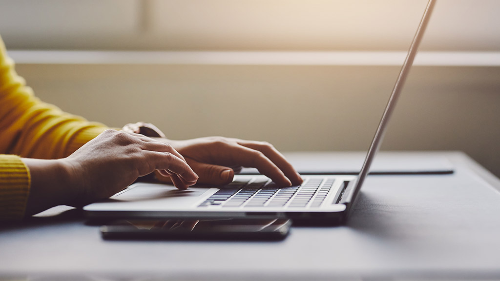 A close-up of a person's hands typing on a laptop keyboard.