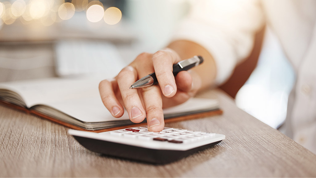 A small business owner uses a calculator and notepad to review a website quote at their desk.